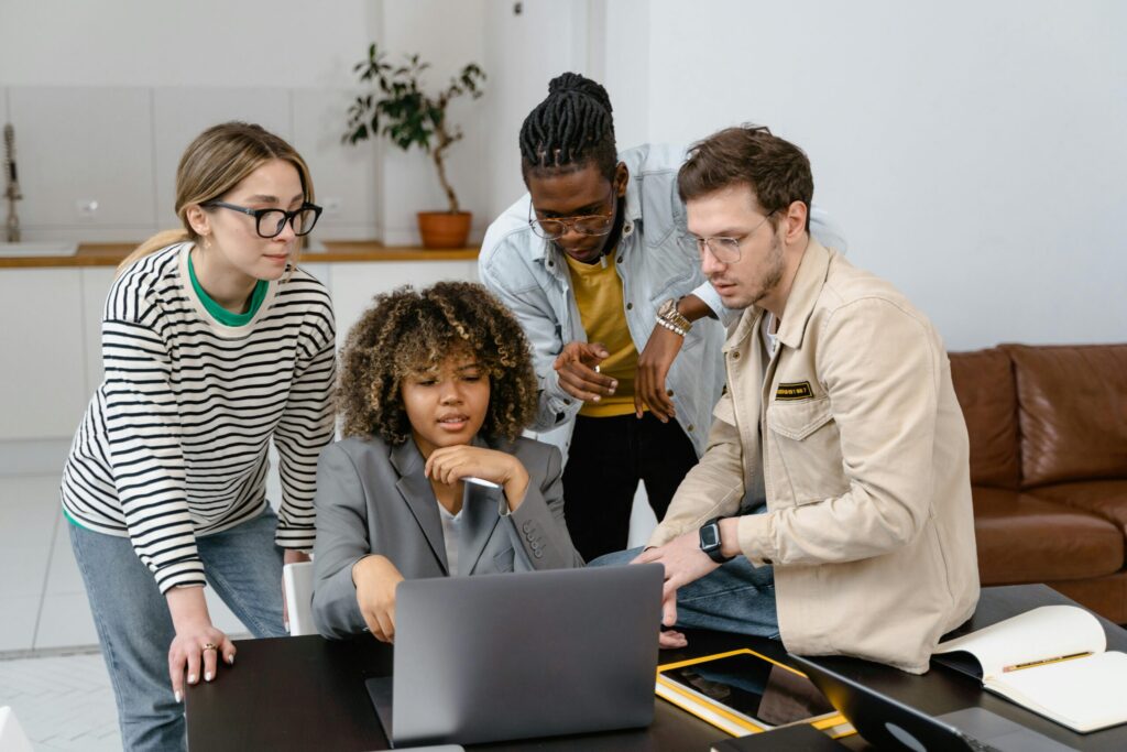 A group of diverse colleagues working together on a project around a laptop.